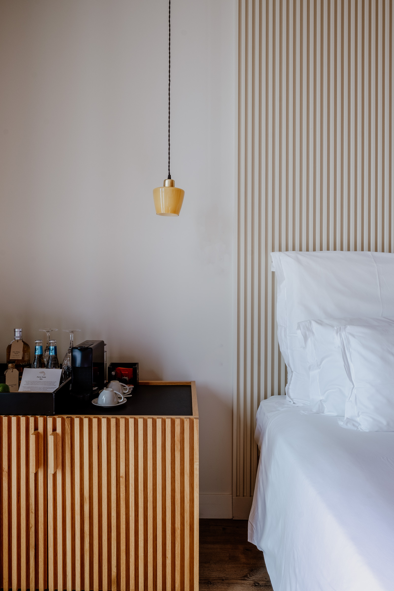 A modern hotel room featuring a wooden accent wall, a neatly made bed with white linens, and a stylish bedside table with a pendant light.