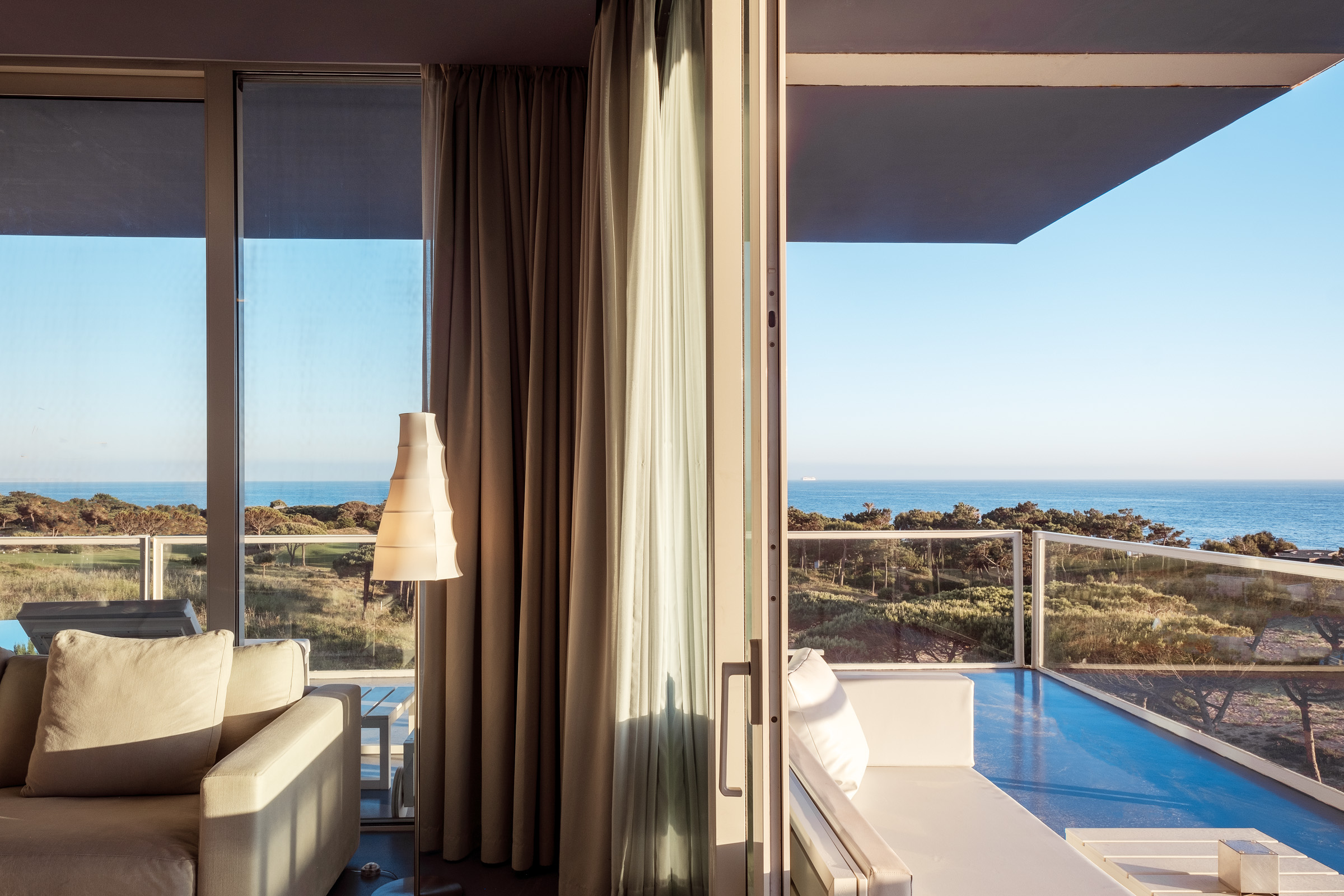 A modern interior view of a coastal living room with a white sofa, large glass windows, and a serene ocean view in the background.
