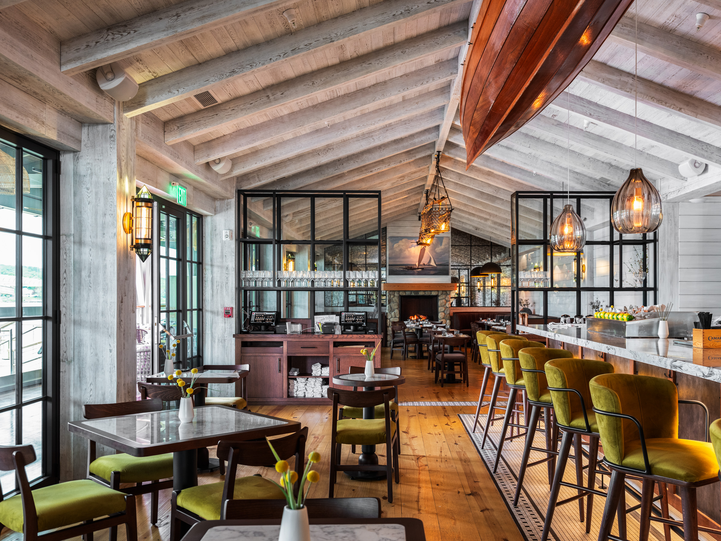 Interior view of a modern restaurant featuring wooden beams, stylish bar stools, and a warm ambiance with hanging lights and a boat decoration.