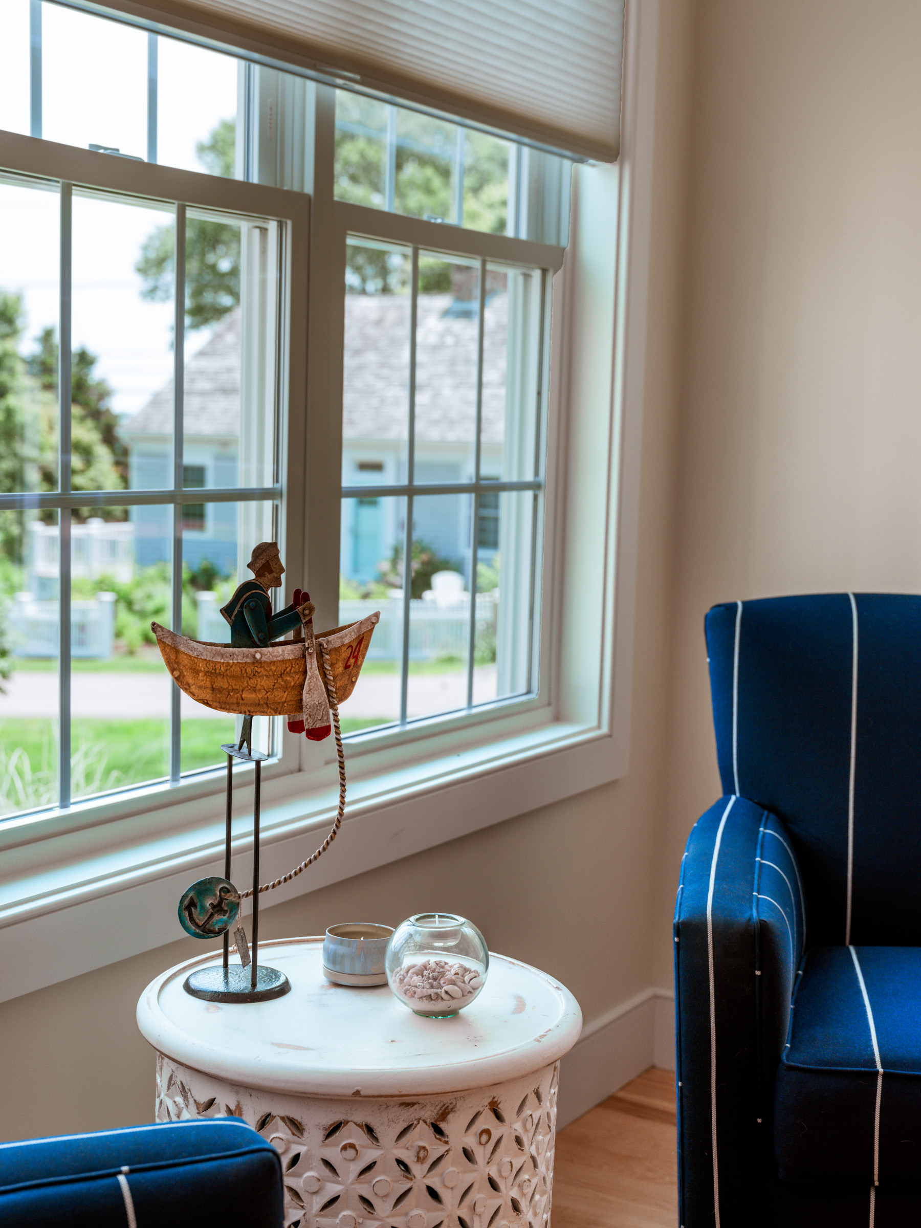 A cozy interior scene featuring a decorative fisherman figurine in a boat on a table near a window, with blue striped chairs and natural light illuminating the space.