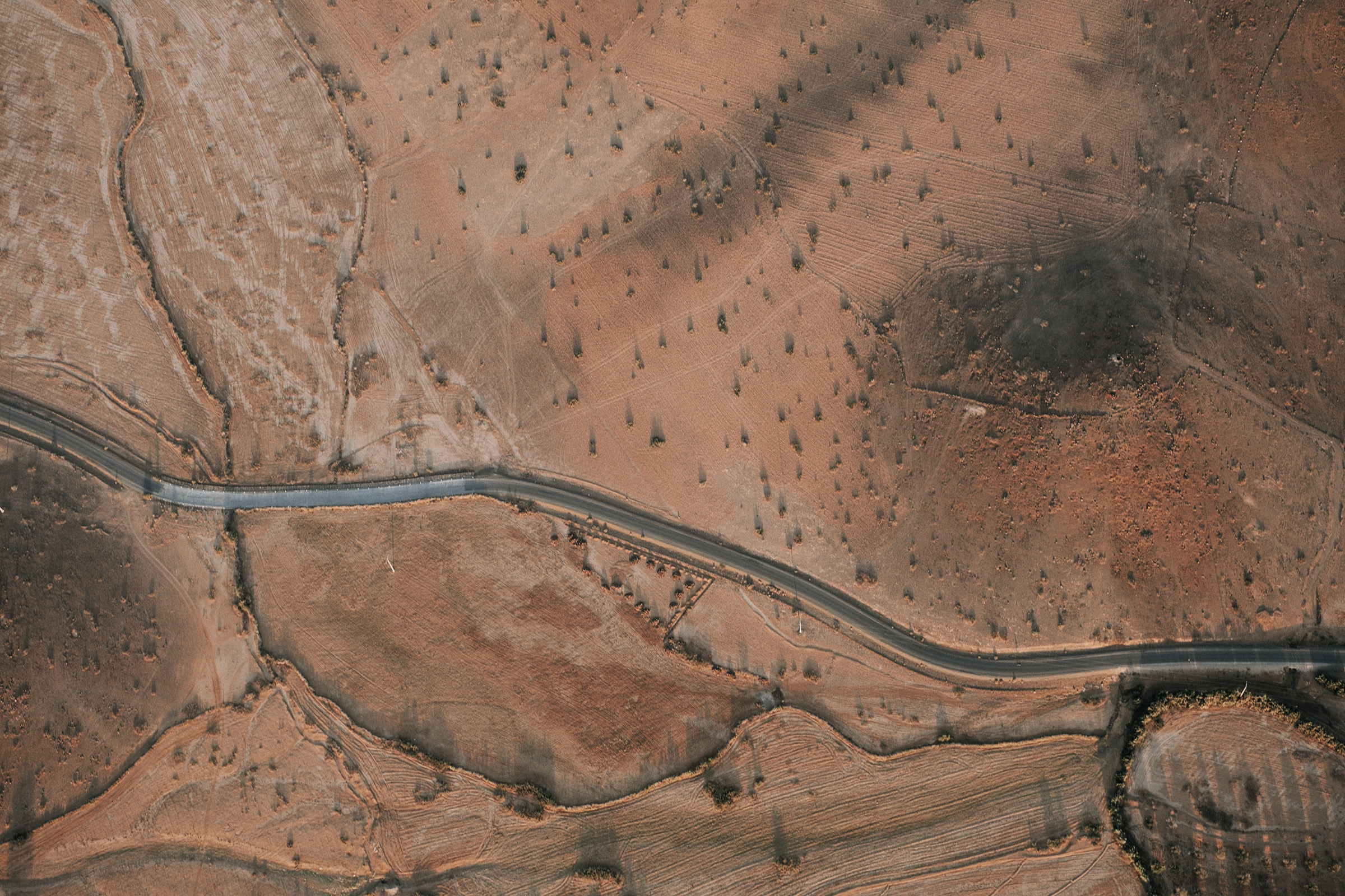 Aerial view of a winding road through arid, textured landscapes with sparse vegetation and earthy tones.