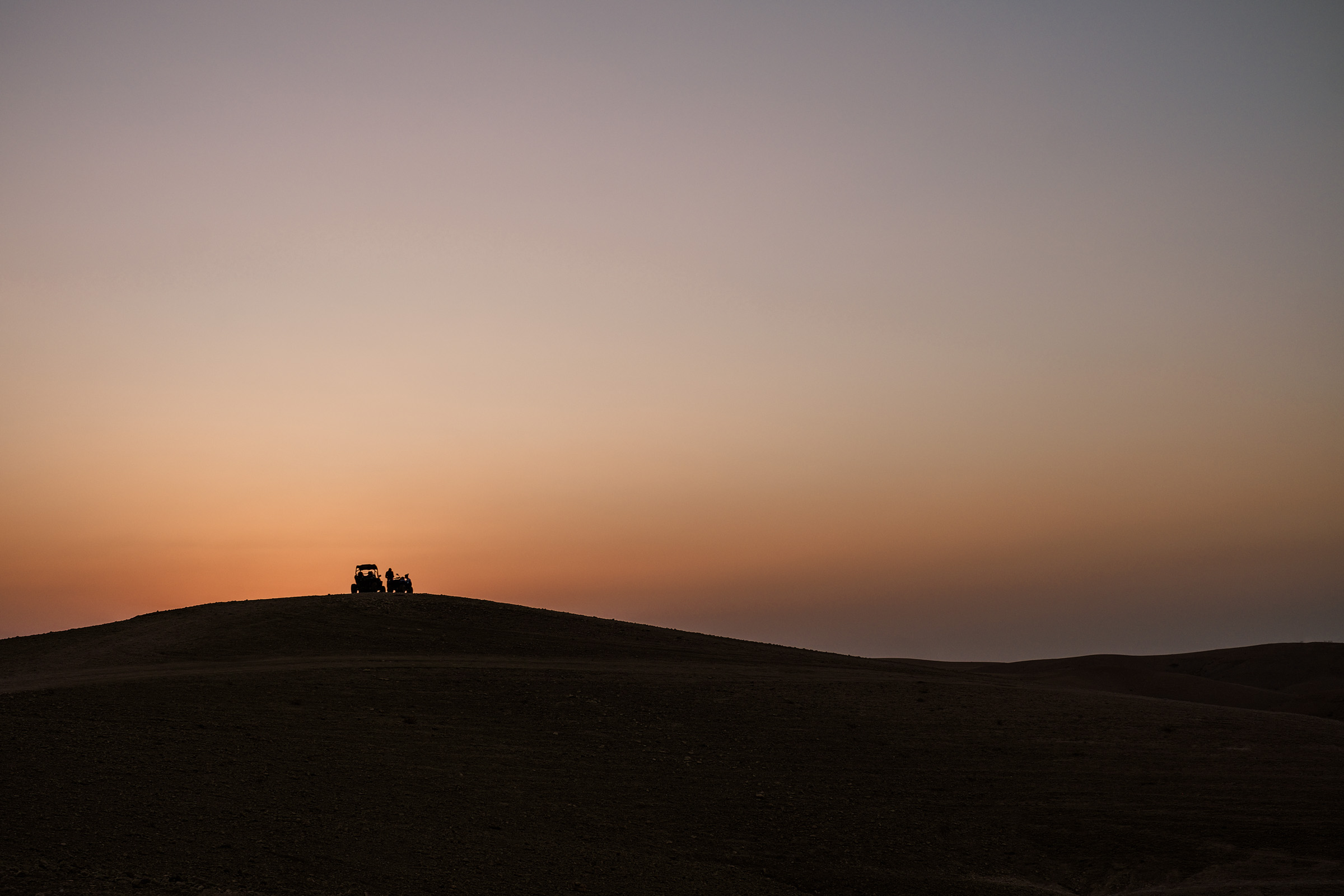 A silhouette of a group of people and a vehicle on a hill at sunset, with a gradient sky transitioning from orange to blue.